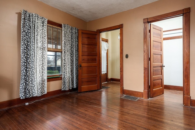 empty room featuring baseboards, a textured ceiling, visible vents, and wood finished floors