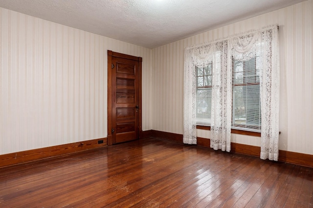 empty room featuring a textured ceiling, hardwood / wood-style floors, and baseboards