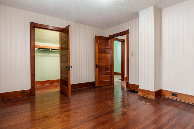 unfurnished bedroom with wallpapered walls, a textured ceiling, baseboards, and hardwood / wood-style flooring