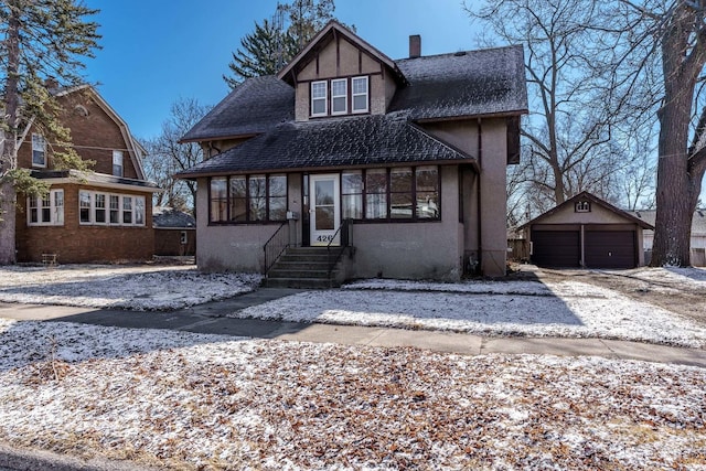 view of front of house with a garage, a chimney, roof with shingles, an outdoor structure, and stucco siding