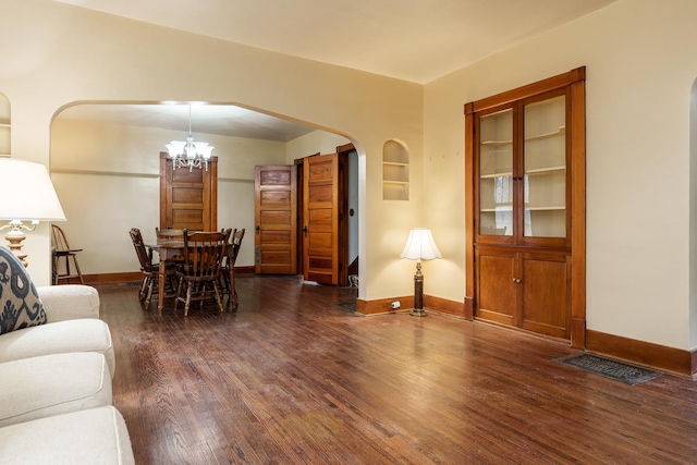 living room featuring arched walkways, an inviting chandelier, baseboards, and wood finished floors