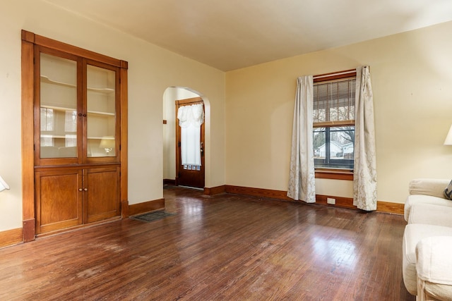 unfurnished living room with arched walkways, wood-type flooring, and baseboards