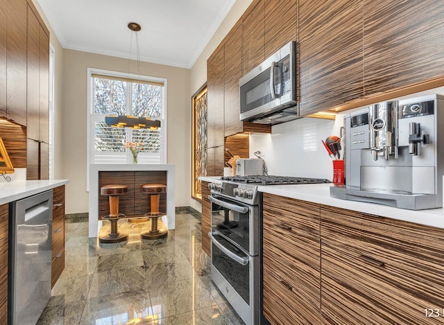 kitchen featuring brown cabinetry, modern cabinets, stainless steel appliances, crown molding, and light countertops