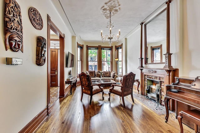 sitting room featuring baseboards, hardwood / wood-style floors, a fireplace, and a notable chandelier