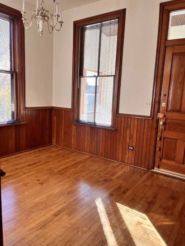 unfurnished dining area with a wainscoted wall, wood walls, plenty of natural light, and light wood-style floors