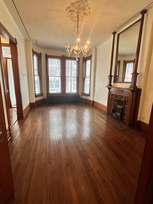 unfurnished living room featuring radiator, an inviting chandelier, dark wood-type flooring, a tile fireplace, and baseboards