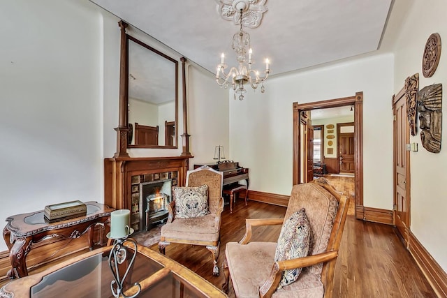 sitting room with an inviting chandelier, a warm lit fireplace, baseboards, and wood finished floors