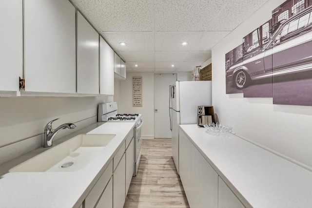 kitchen featuring white appliances, light wood-style flooring, light countertops, white cabinetry, and a sink