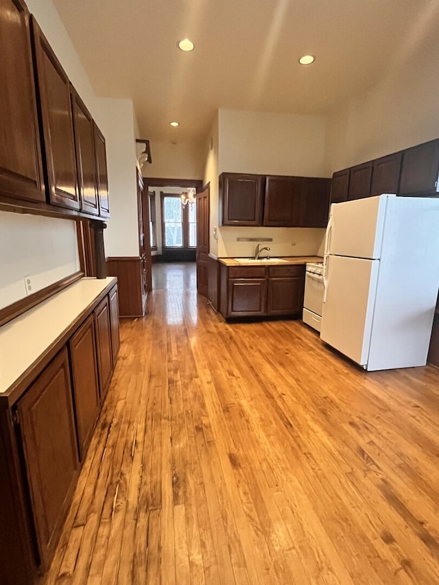 kitchen with dark brown cabinetry, white appliances, light wood-style flooring, and a sink