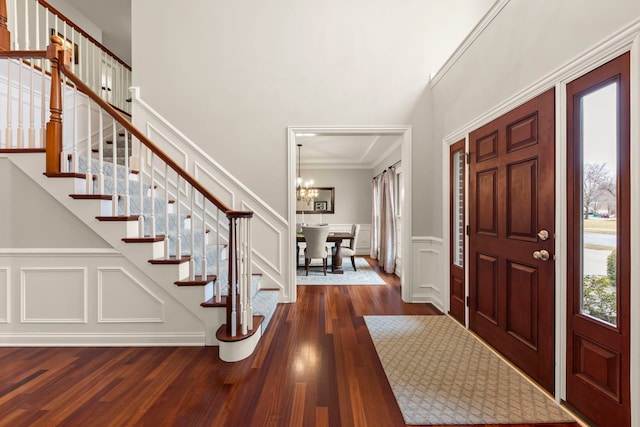 entryway featuring a notable chandelier, dark wood finished floors, a decorative wall, a high ceiling, and stairs