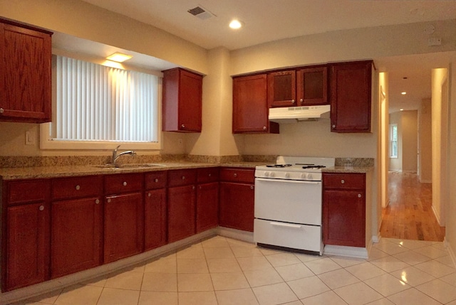 kitchen featuring gas range gas stove, light tile patterned floors, visible vents, a sink, and under cabinet range hood