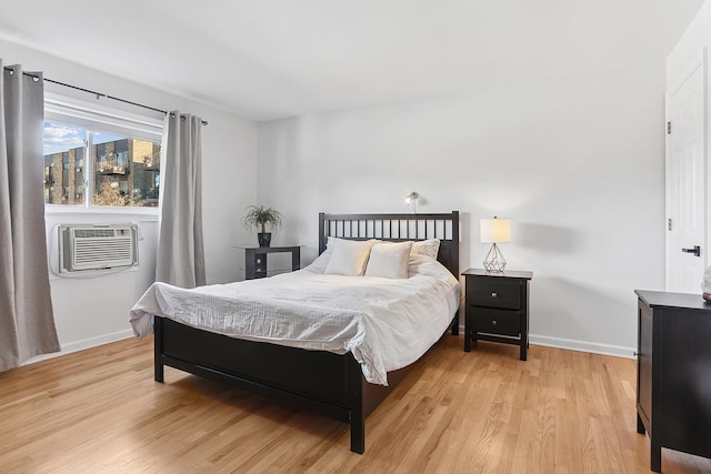 bedroom with light wood-style flooring, a wall mounted AC, and baseboards