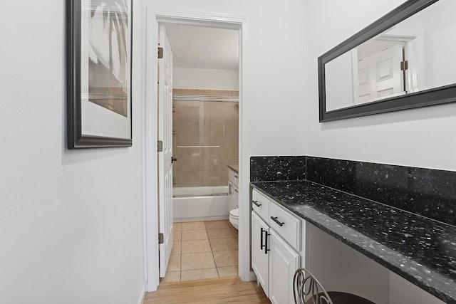 bathroom featuring bath / shower combo with glass door, toilet, vanity, and tile patterned flooring