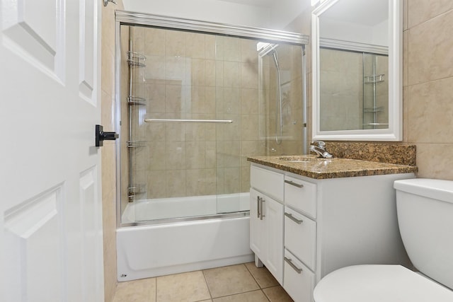 bathroom with toilet, tile walls, tile patterned flooring, enclosed tub / shower combo, and vanity