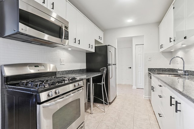 kitchen with a sink, dark stone countertops, stainless steel appliances, light tile patterned floors, and decorative backsplash