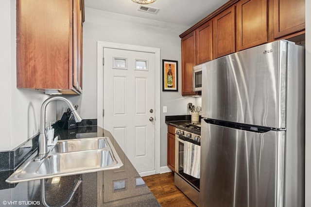 kitchen with stainless steel appliances, dark countertops, visible vents, brown cabinetry, and a sink