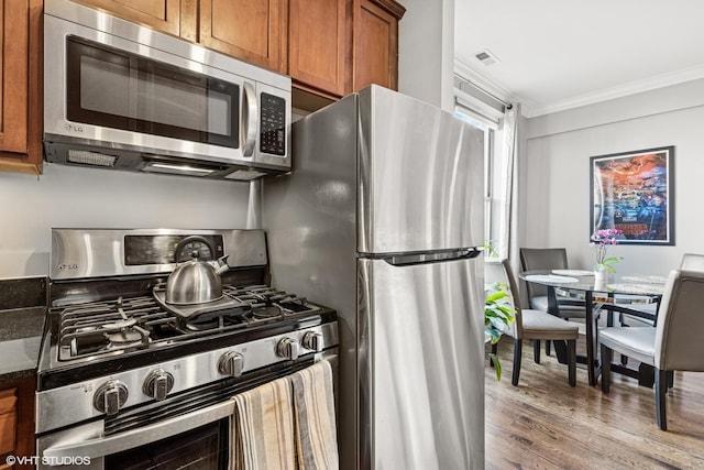 kitchen with visible vents, brown cabinets, wood finished floors, stainless steel appliances, and crown molding