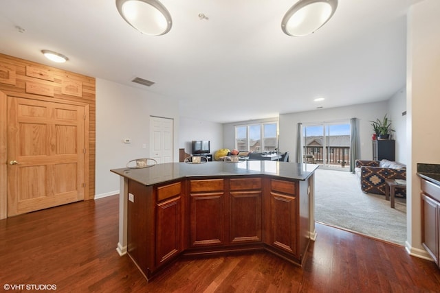 kitchen with dark countertops, visible vents, a kitchen island, open floor plan, and dark wood-style flooring