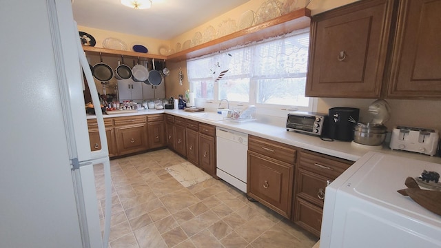 kitchen featuring a toaster, white appliances, a sink, light countertops, and washer / clothes dryer