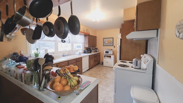 kitchen featuring brown cabinets, light countertops, a sink, white appliances, and under cabinet range hood