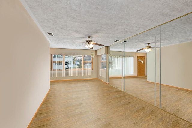 empty room featuring light wood-type flooring, a textured ceiling, visible vents, and a ceiling fan