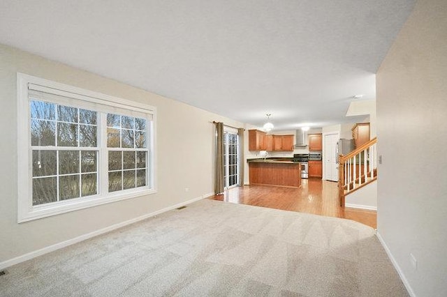 interior space featuring stainless steel gas range oven, baseboards, dark countertops, open floor plan, and wall chimney range hood