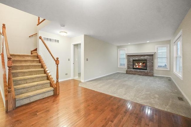 unfurnished living room featuring a brick fireplace, wood-type flooring, visible vents, and baseboards