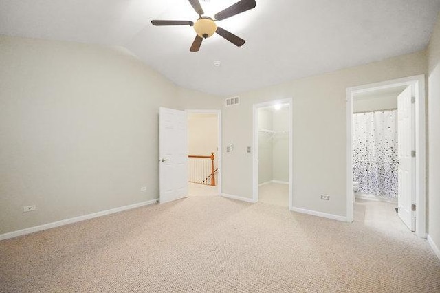 unfurnished bedroom featuring light carpet, baseboards, a spacious closet, vaulted ceiling, and a closet