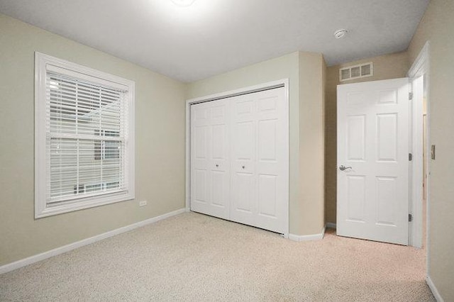 unfurnished bedroom featuring baseboards, visible vents, a closet, and light colored carpet