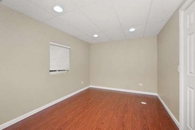 empty room with baseboards, a drop ceiling, wood finished floors, and recessed lighting