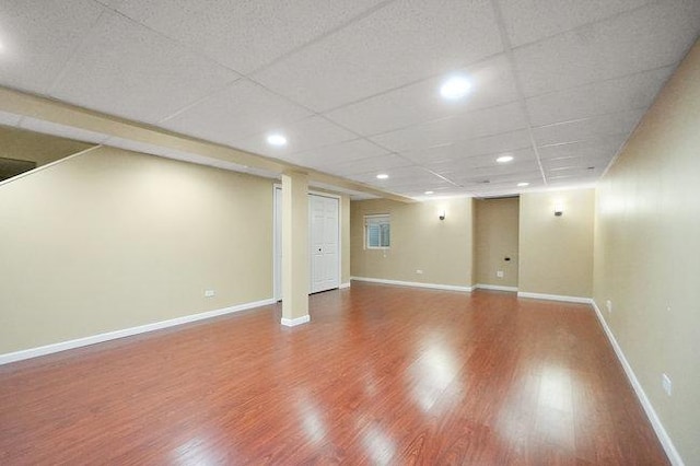 finished basement with a paneled ceiling, baseboards, wood finished floors, and recessed lighting