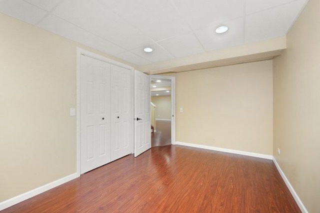 unfurnished bedroom with baseboards, a drop ceiling, and wood finished floors