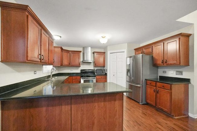 kitchen with dark wood finished floors, wall chimney exhaust hood, a peninsula, stainless steel appliances, and a sink