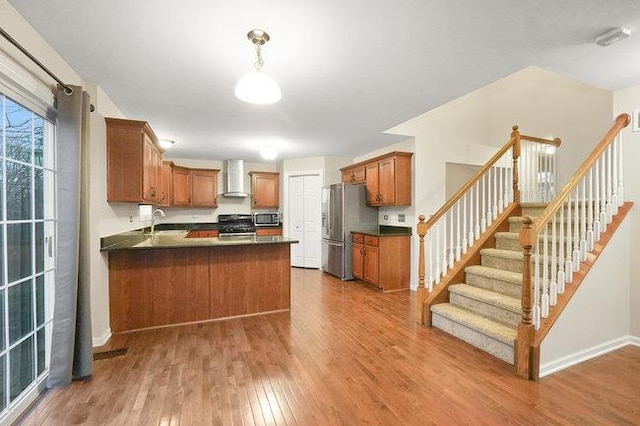 kitchen featuring dark countertops, wall chimney exhaust hood, appliances with stainless steel finishes, wood finished floors, and a peninsula