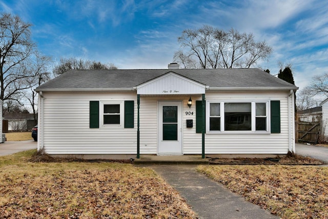 bungalow-style house with a chimney, fence, and roof with shingles