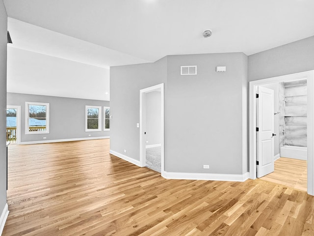 unfurnished living room with vaulted ceiling, light wood-style flooring, visible vents, and baseboards