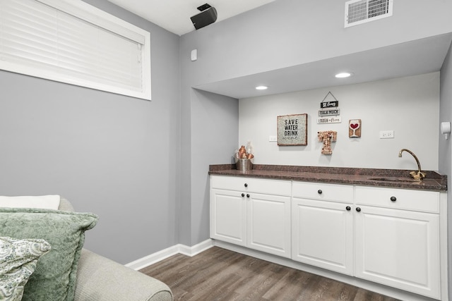 bar with visible vents, dark wood-type flooring, a sink, wet bar, and baseboards