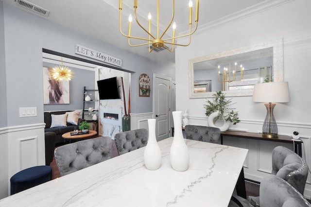 dining space with visible vents, a decorative wall, ornamental molding, a large fireplace, and wainscoting