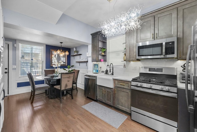 kitchen featuring a notable chandelier, wood finished floors, a sink, appliances with stainless steel finishes, and open shelves