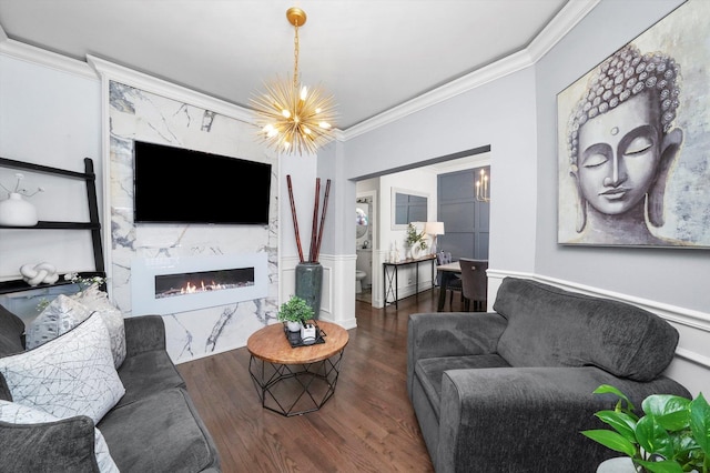 living room featuring a wainscoted wall, crown molding, a premium fireplace, an inviting chandelier, and wood finished floors