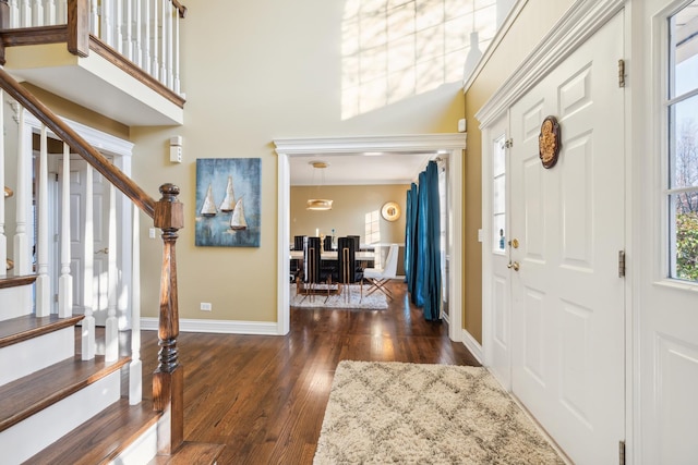 foyer entrance with dark wood-type flooring, a towering ceiling, baseboards, and stairs