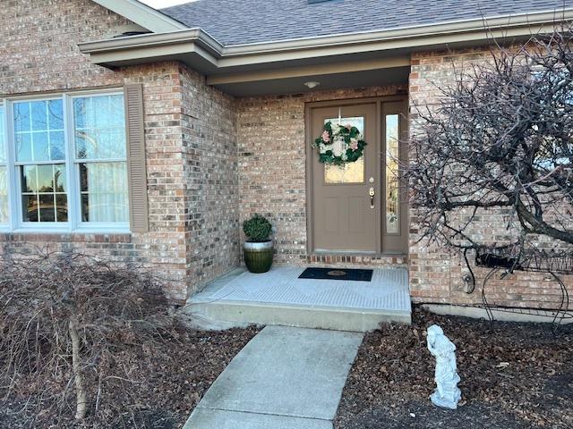 view of exterior entry with brick siding and roof with shingles