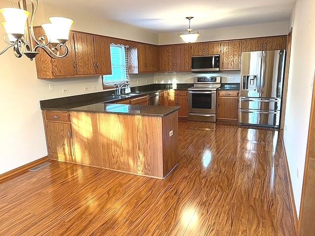 kitchen featuring a peninsula, dark countertops, stainless steel appliances, and a sink