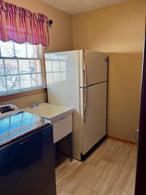 kitchen featuring light countertops, a sink, freestanding refrigerator, and baseboards