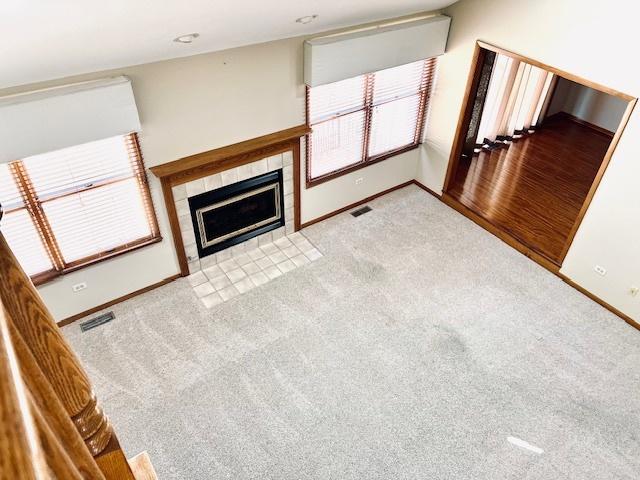 unfurnished living room featuring light colored carpet, visible vents, baseboards, and a tile fireplace