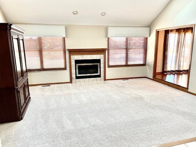 unfurnished living room with lofted ceiling, light carpet, baseboards, and a tiled fireplace