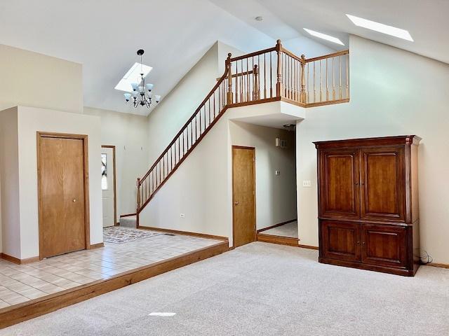 foyer with a skylight, stairway, carpet, high vaulted ceiling, and a notable chandelier