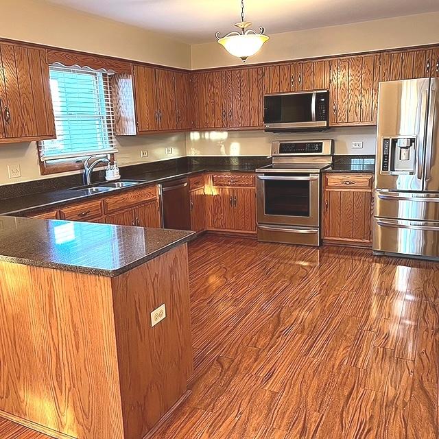 kitchen featuring stainless steel appliances, dark wood-type flooring, brown cabinetry, and a sink