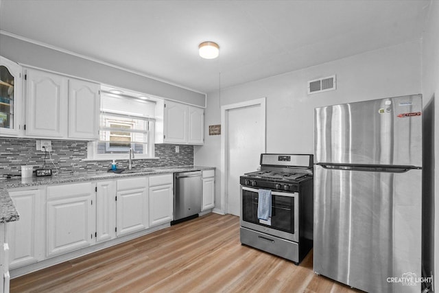 kitchen featuring visible vents, white cabinets, light stone countertops, stainless steel appliances, and a sink