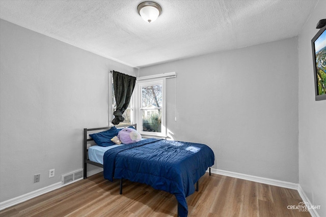 bedroom with baseboards, visible vents, and wood finished floors